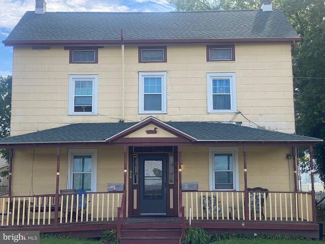 view of front of house featuring a porch, a shingled roof, and a chimney