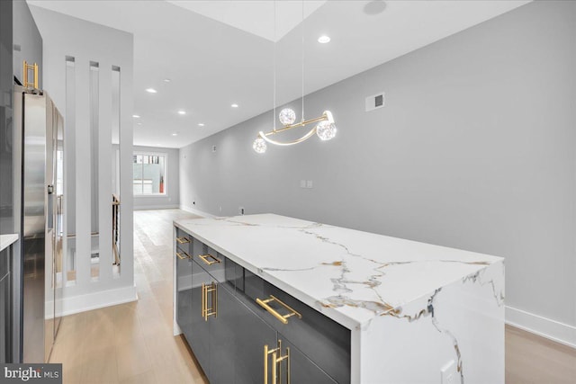 interior space with light stone countertops, stainless steel fridge, light wood-type flooring, a kitchen island, and hanging light fixtures