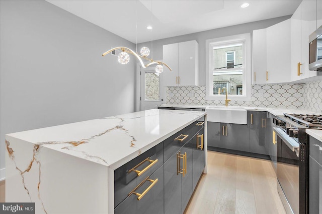 kitchen featuring white cabinets, light stone countertops, light wood-type flooring, decorative light fixtures, and stainless steel appliances