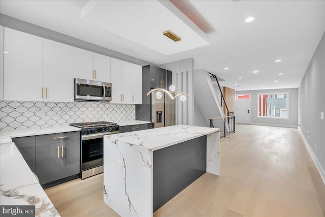 kitchen featuring white cabinetry, stainless steel appliances, decorative light fixtures, and light hardwood / wood-style floors