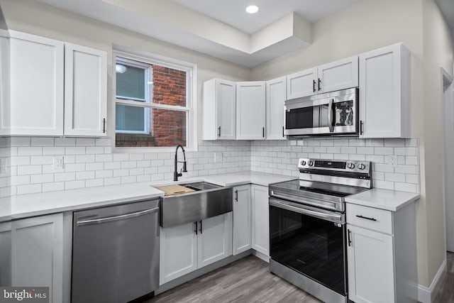 kitchen with light wood-type flooring, sink, white cabinetry, decorative backsplash, and stainless steel appliances