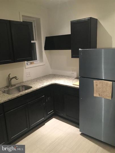 kitchen with stainless steel refrigerator, sink, and light stone countertops