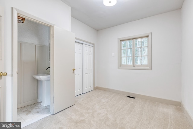 unfurnished bedroom featuring a closet, ensuite bath, and light carpet