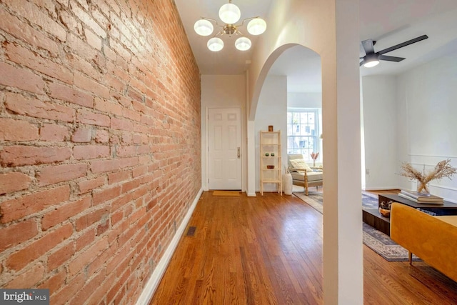 hall featuring brick wall, hardwood / wood-style flooring, and a notable chandelier