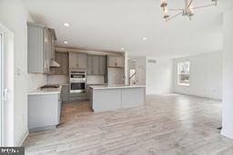 kitchen featuring tasteful backsplash, a kitchen island, double oven, gray cabinets, and light wood-type flooring