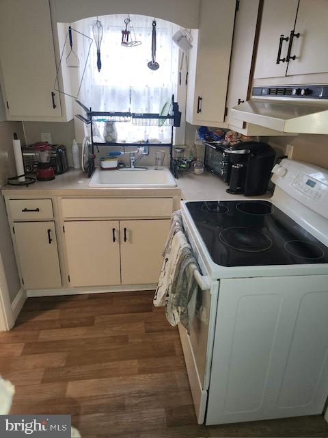 kitchen with sink, range hood, white cabinetry, hanging light fixtures, and white range with electric cooktop