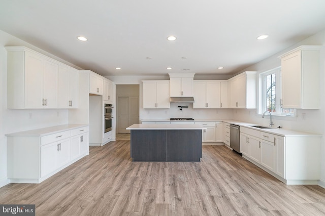 kitchen featuring appliances with stainless steel finishes, light wood-type flooring, a center island, white cabinets, and sink