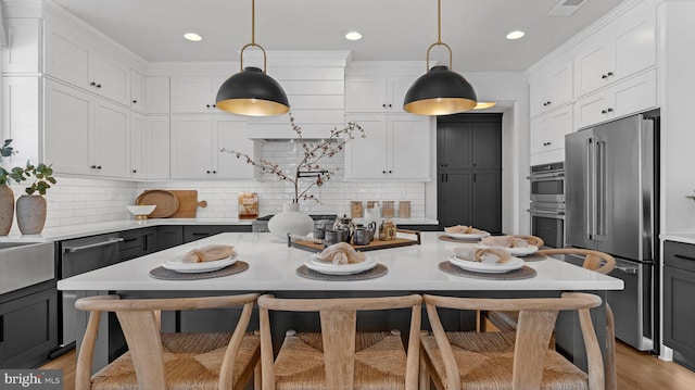 kitchen with appliances with stainless steel finishes, pendant lighting, white cabinetry, and backsplash