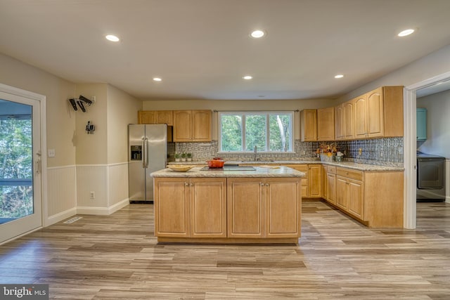 kitchen with a kitchen island, washer / dryer, stainless steel refrigerator with ice dispenser, sink, and light hardwood / wood-style floors