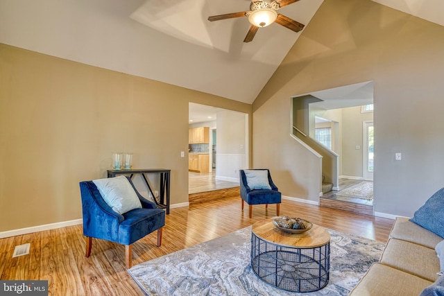 living area featuring wood finished floors, stairway, baseboards, high vaulted ceiling, and a ceiling fan