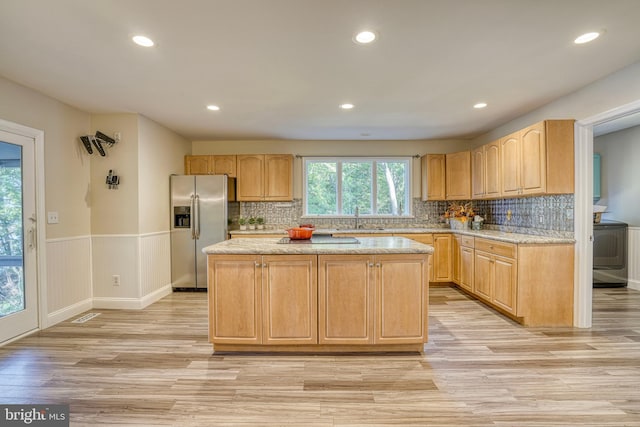 kitchen featuring sink, a center island, light stone counters, light hardwood / wood-style flooring, and stainless steel refrigerator with ice dispenser