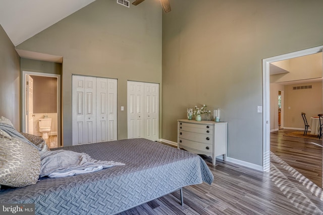 bedroom with high vaulted ceiling, ceiling fan, connected bathroom, hardwood / wood-style flooring, and two closets