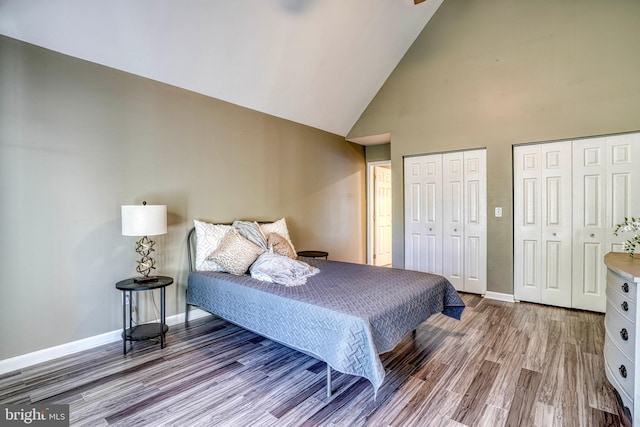 bedroom featuring light hardwood / wood-style flooring, two closets, and high vaulted ceiling