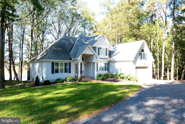 traditional-style home with roof with shingles, gravel driveway, a front yard, and a garage
