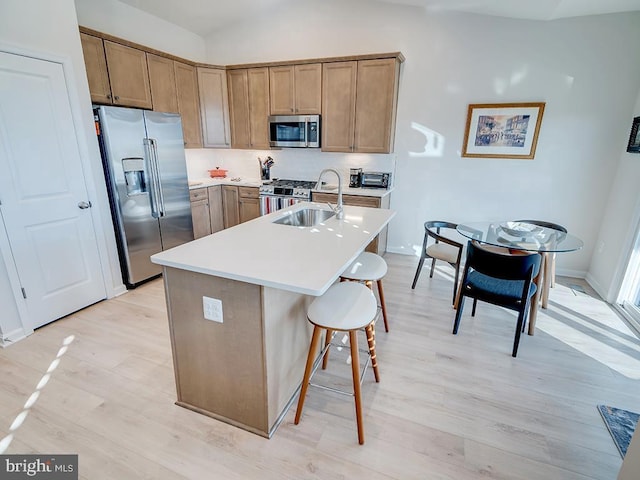 kitchen with appliances with stainless steel finishes, a breakfast bar area, light wood-type flooring, a kitchen island with sink, and sink