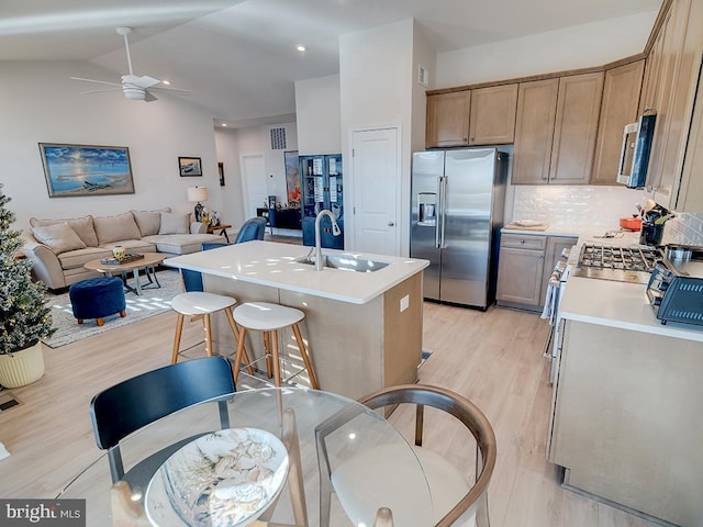 kitchen featuring sink, tasteful backsplash, a kitchen island with sink, stainless steel appliances, and light wood-type flooring