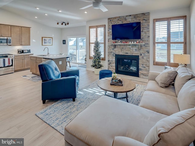 living room featuring ceiling fan, a stone fireplace, light wood-type flooring, and sink