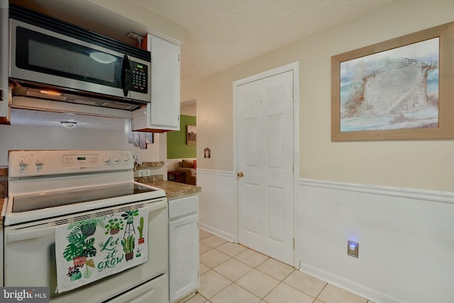 kitchen with white electric stove, a textured ceiling, light tile patterned floors, and white cabinets