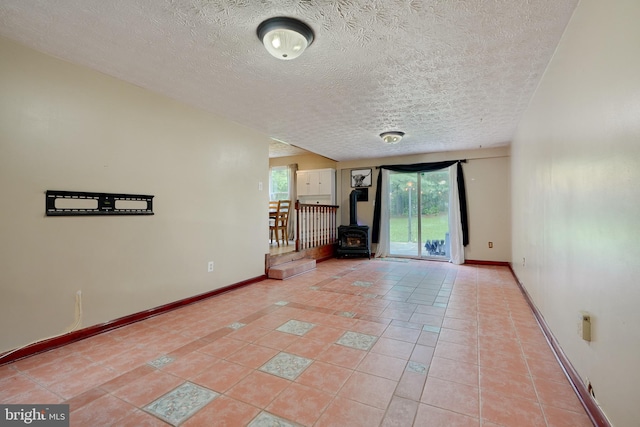 unfurnished living room with a wood stove, light tile patterned flooring, and a textured ceiling