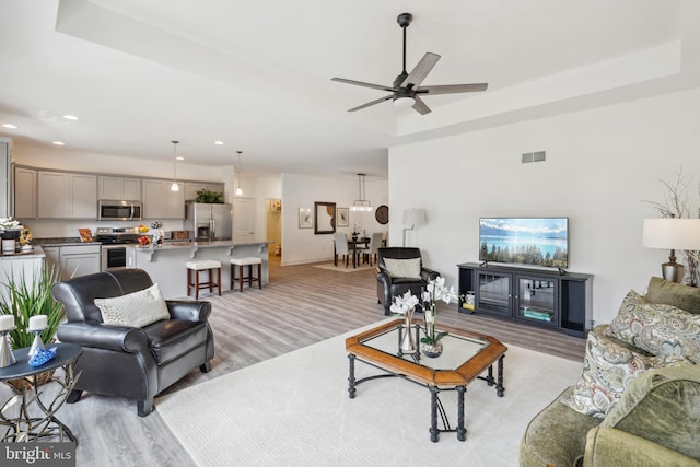 living room featuring ceiling fan with notable chandelier, light hardwood / wood-style floors, and a raised ceiling