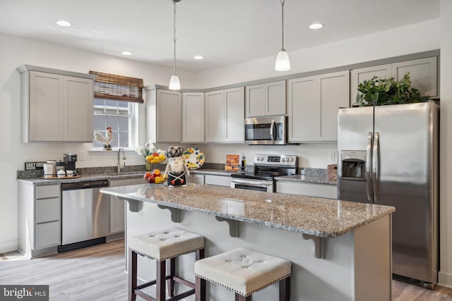 kitchen featuring light stone counters, stainless steel appliances, light wood-type flooring, a center island, and decorative light fixtures