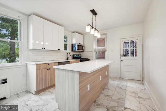 kitchen featuring radiator heating unit, a kitchen island, stainless steel appliances, hanging light fixtures, and white cabinetry