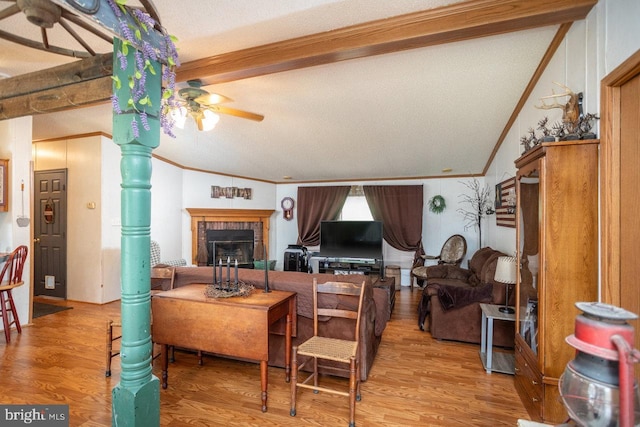 living area featuring a brick fireplace, lofted ceiling with beams, a ceiling fan, crown molding, and wood finished floors