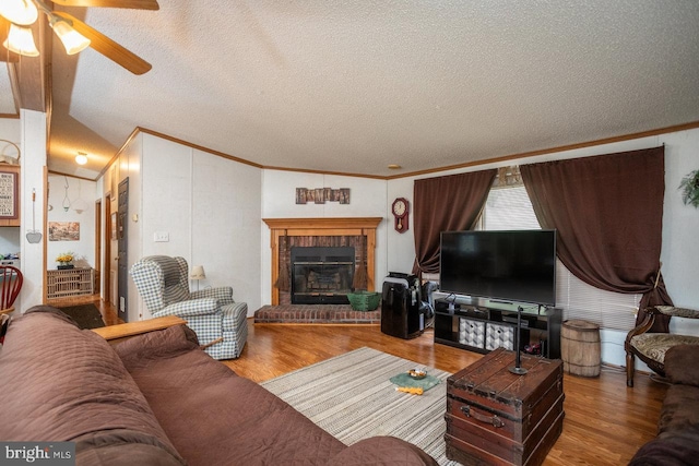 living room with a textured ceiling, a fireplace, hardwood / wood-style floors, ornamental molding, and ceiling fan