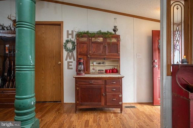 kitchen featuring light wood-type flooring, vaulted ceiling, a textured ceiling, and crown molding