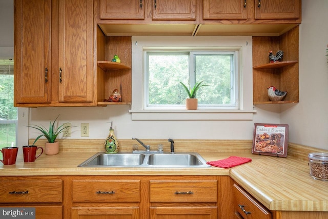 kitchen featuring light countertops, a sink, open shelves, and brown cabinetry