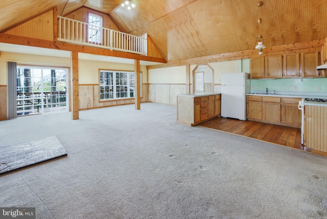 unfurnished living room with light wood-type flooring, wood walls, sink, and high vaulted ceiling