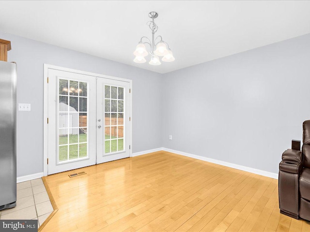 dining space featuring light wood-type flooring, an inviting chandelier, and french doors