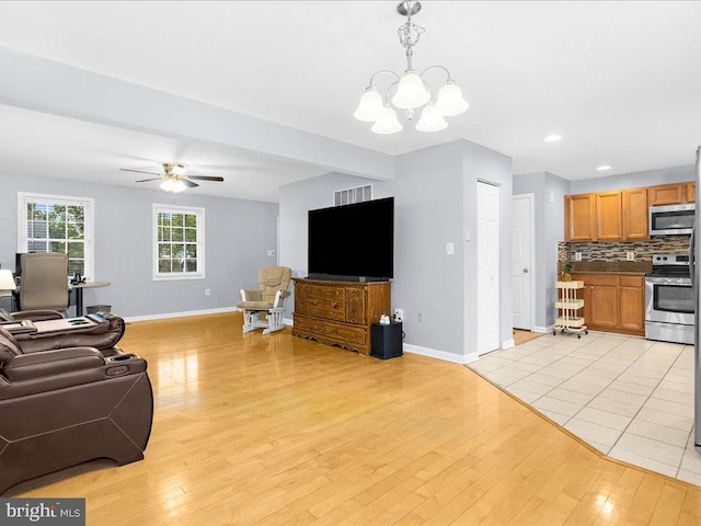 living room featuring ceiling fan with notable chandelier and light wood-type flooring