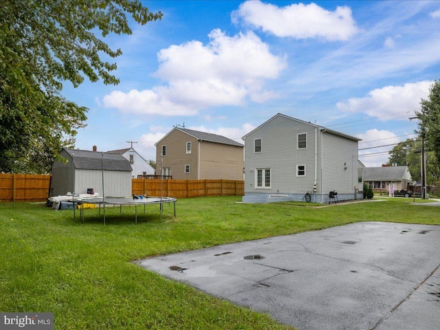 rear view of property featuring a lawn, a patio, a shed, and a trampoline