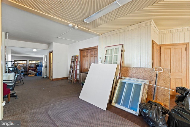 miscellaneous room featuring wooden walls and dark colored carpet