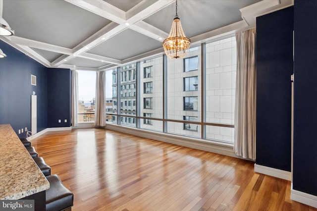 unfurnished dining area featuring beamed ceiling, coffered ceiling, light hardwood / wood-style flooring, and a notable chandelier