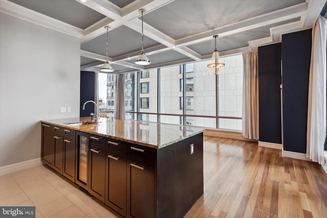 kitchen with light stone counters, sink, decorative light fixtures, coffered ceiling, and light wood-type flooring