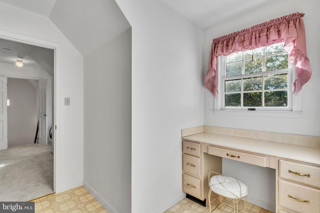 office area featuring lofted ceiling, built in desk, and light carpet