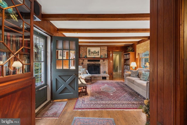 living room with a brick fireplace, beam ceiling, plenty of natural light, and light hardwood / wood-style floors