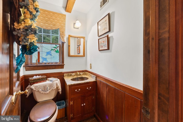 bathroom featuring vanity, wood walls, toilet, and beam ceiling