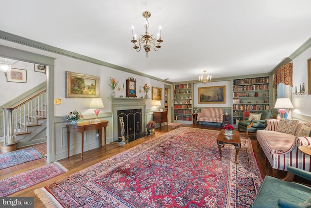 living room with ornamental molding, an inviting chandelier, built in features, and hardwood / wood-style floors