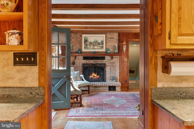 living room featuring a brick fireplace, beam ceiling, and light hardwood / wood-style flooring