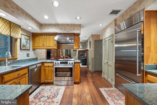 kitchen featuring high quality appliances, dark wood-type flooring, range hood, sink, and kitchen peninsula