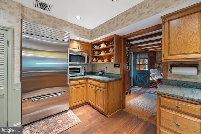 kitchen featuring appliances with stainless steel finishes, beam ceiling, light hardwood / wood-style floors, and dark stone counters