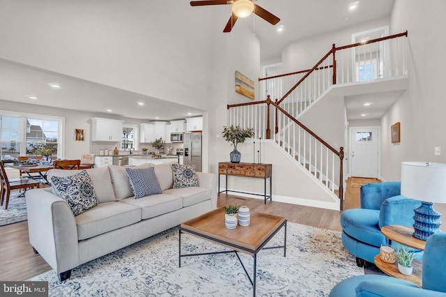 living room with ceiling fan, a towering ceiling, and light hardwood / wood-style floors