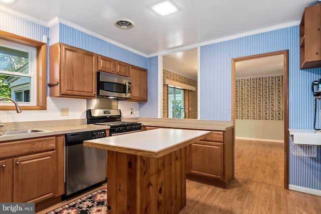 kitchen featuring appliances with stainless steel finishes, light hardwood / wood-style flooring, sink, crown molding, and a center island