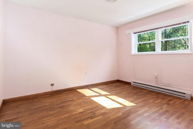 empty room with hardwood / wood-style flooring and a baseboard heating unit