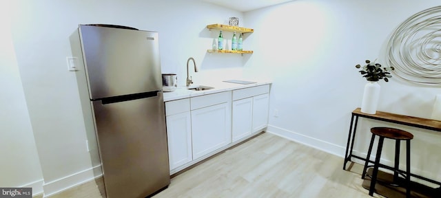 bar featuring white cabinets, stainless steel fridge, light wood-type flooring, and sink