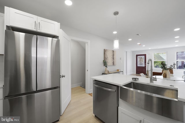 kitchen featuring stainless steel appliances, sink, decorative light fixtures, white cabinets, and light hardwood / wood-style floors