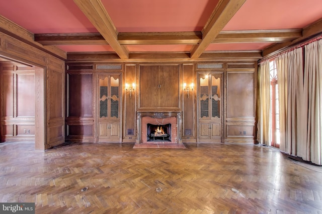 unfurnished living room featuring beamed ceiling, coffered ceiling, wooden walls, a decorative wall, and a premium fireplace